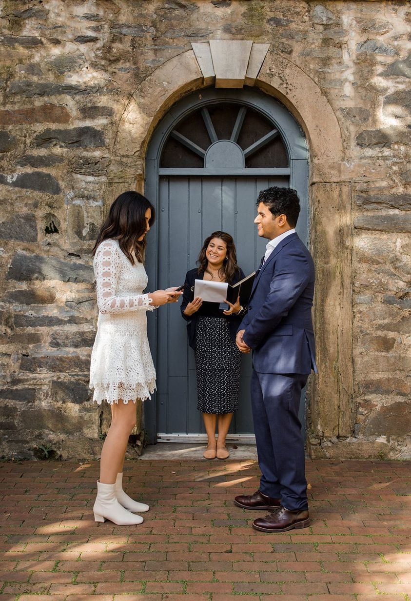 Couple exchanging vows during an intimate elopement ceremony in front of a stone building with an arched blue door