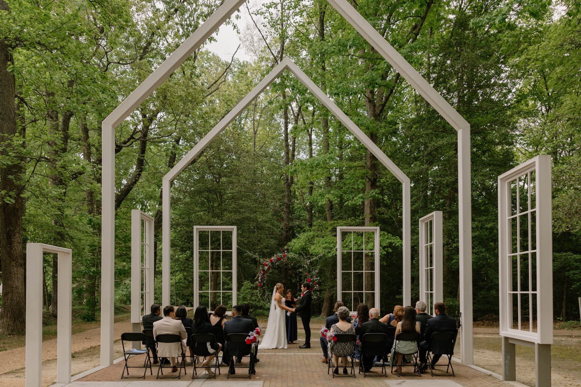 Outdoor micro wedding ceremony inside a white open-air chapel frame surrounded by green forest