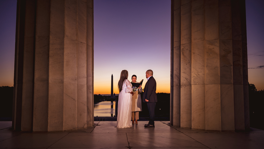 Couple exchanging vows at sunrise between the marble columns of the Lincoln Memorial with the Washington Monument in the distance